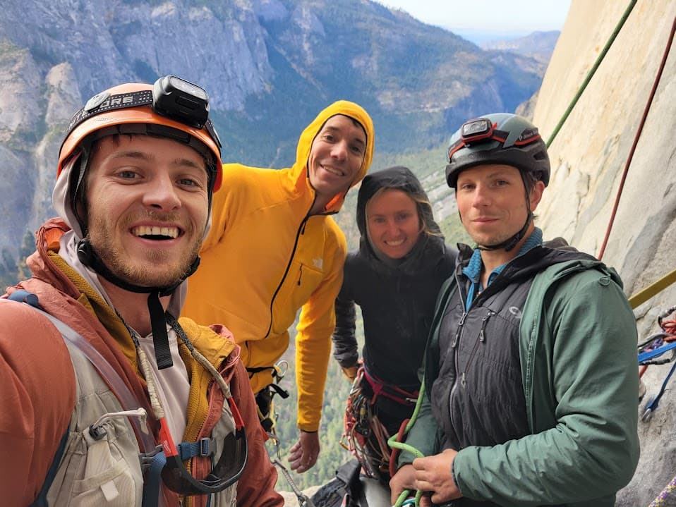 Caleb and friends, including Alex Honnold, grinning on a portaledge bivy high on a Yosemite big wall